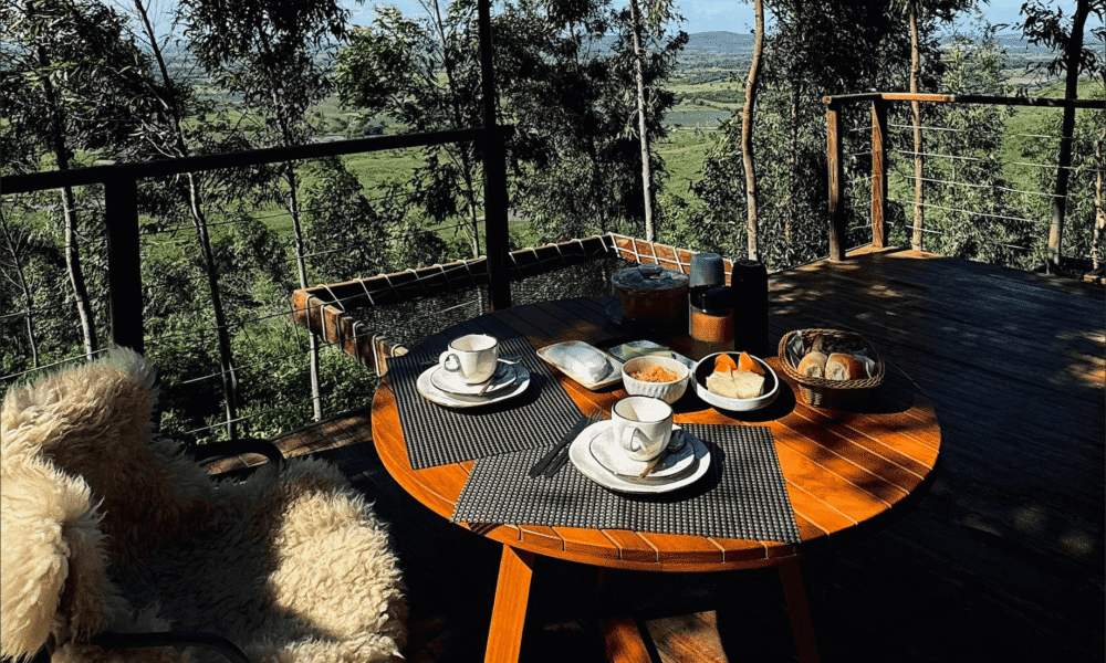 Cozy outdoor dining setup on a balcony overlooking lush forest and distant hills.