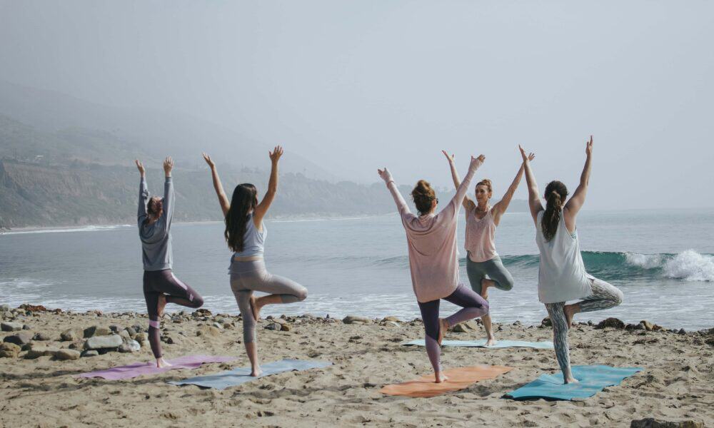 Group practicing yoga on the beach during sunrise or sunset.